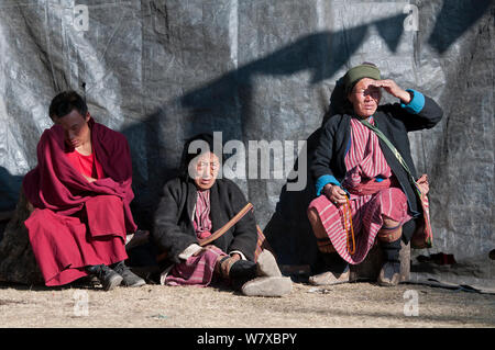 A monk and two ladies in traditional Mompa tribe dress watching the rehearsal of dances in preparation for the Torgya festival. Galdan Namge Lhatse Monastery, Tawang, Arunachal Pradesh, India. January 2014. Stock Photo