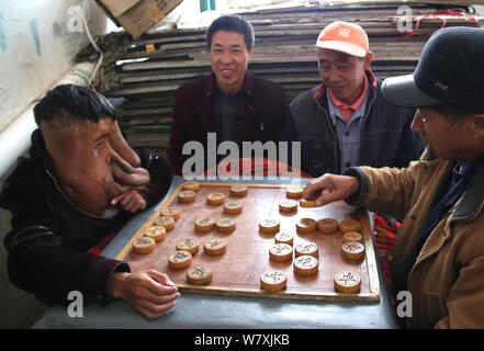 'China's Elephant Man' Huang Chuncai, 41, who suffers from a 15kg huge tumor on the face, plays Chinese chess with villagers at home in Yulan village, Stock Photo