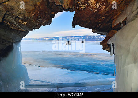 View through rock arch of vehicles parked on ice on the surface of Lake Baikal, Siberia, Russia, March 2012. Stock Photo