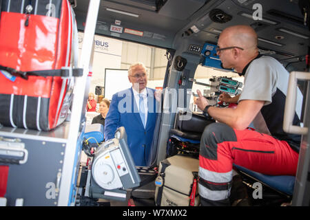 07 August 2019, Bavaria, Munich: Joachim Herrmann (CSU), Bavarian Minister of the Interior, asks Andreas Bayer of the DRF Luftrettung to explain the equipment of the Airbus helicopter H145 of the DRF Luftrettung. Someone is seriously injured in an accident or suffers a heart attack - if quick help from the air is required, one of the rescue or intensive transport helicopters stationed in Bavaria takes off. The balance sheet for 2018 is now available. Photo: Sina Schuldt/dpa Stock Photo