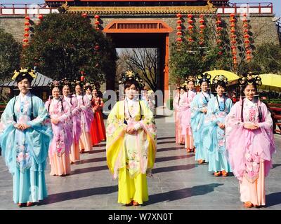 Chinese tour guides dressed in traditional Han costumes bite chopsticks to practice smiling for tourists at the Millennium City Park, a tourist attrac Stock Photo