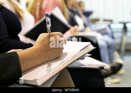 Women sitting in a row in a conference room, female hand with pen writing in a notepad. Concept of lecture, business meeting, college classes, skills Stock Photo