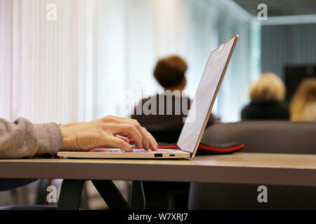 Woman using laptop in office, female hands on a keyboard. Girl sitting with a notebook with closed camera at a table on people background Stock Photo