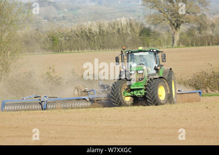 Buckingham, UK - April 01, 2019. A farmer drives a John Deere tractor to cultivate land during a drought, using a Cambridge roller or cultipacker. Stock Photo