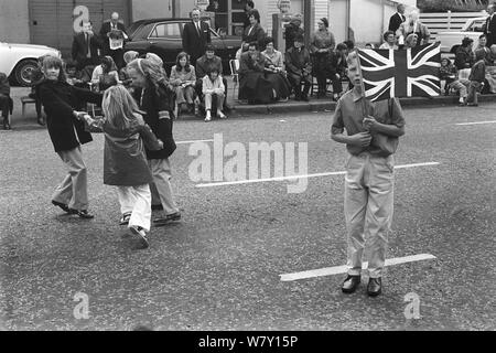 Belfast Orange Day Parade. Protestant children waiting for the parade to come through their neighbourhood. Girls playing Ringa Ringa Rosie, and teen boy with Union Jack flags. July 1970 1970s  HOMER SYKES Stock Photo