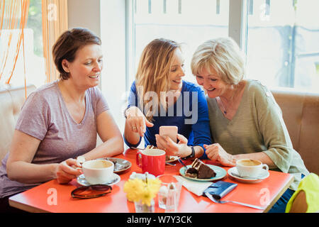 A group of three mature women having coffee and cake; they are looking at one of their phones. Stock Photo