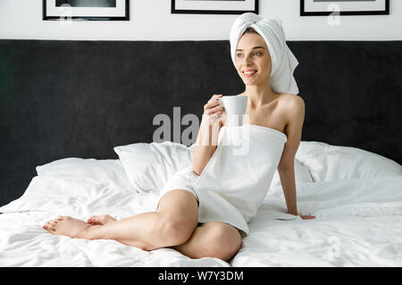 Stylish brunette girl in white towel enjoying morning with hot drink Stock Photo