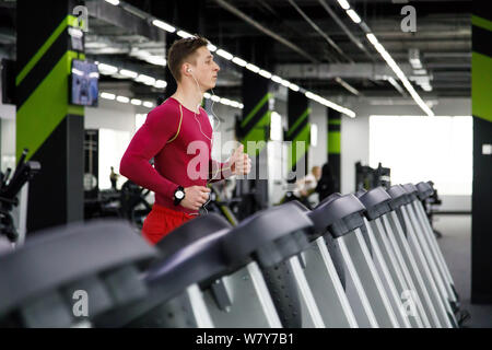 Young sportsman in red sportswear running on treadmill at gym Stock Photo