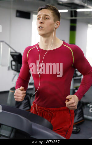 Young man in red sportswear running on treadmill in gym and doing cardio workout Stock Photo