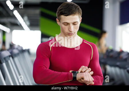 Handsome fitness man using smart watch while standing at the gym Stock Photo