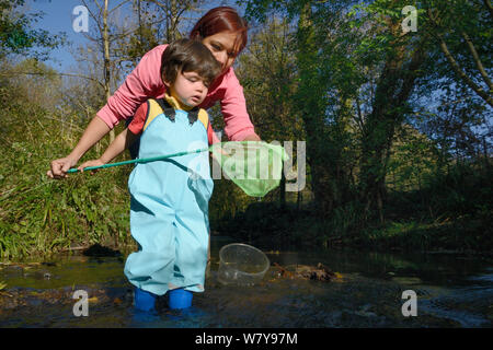 Young boy and his mother fishing net after dipping it into stream, Bristol, UK, October 2014. Model released. Stock Photo