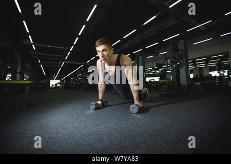 Athletic man doing push-ups with the dumbbells at the gym Stock Photo