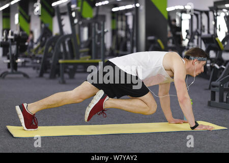 Athletic man in headphones wearing sport outfit doing exercise at the gym Stock Photo