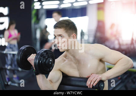 Muscular man working out in gym doing exercises with dumbbells, strong male at the gym Stock Photo