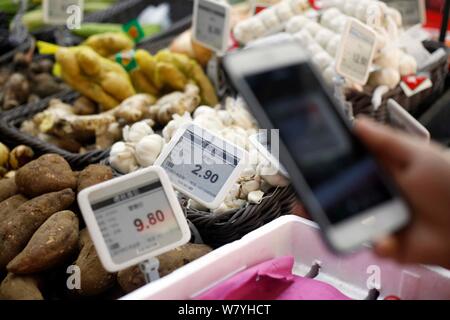 A Chinese customer uses her smartphone to scan the QR code on vegetables at a market in Shanghai, China, 6 March 2017.   A wet market on downtown Huas Stock Photo