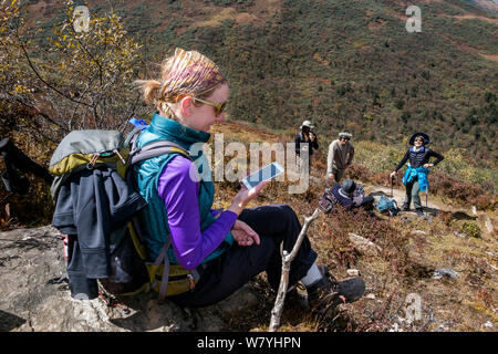 Woman using a mobile phone miles away from any city along the Jhomolhari Trek.  Bhutan, October 2014. Model released. Stock Photo