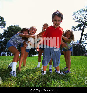 Girls tugging boy Stock Photo
