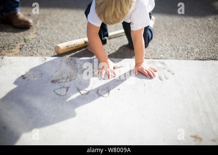 Young boy pressing his hands into wet cement outdoors. Stock Photo