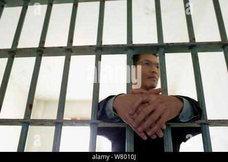 Confident young businessman standing in a empty prison cell behind bars in a derelict building. Stock Photo