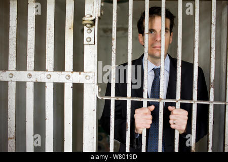 Portrait of a confident young businessman standing in a empty prison cell behind bars in a derelict building. Stock Photo