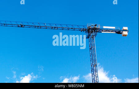 a crane lifting weights on a construction site with a blue sky and clouds on the background. construction and construction engineering. Stock Photo