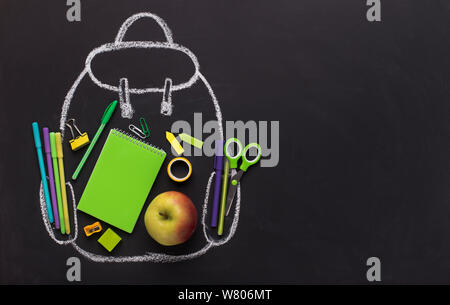 Green school stationery inside chalk painted backpack on black Stock Photo