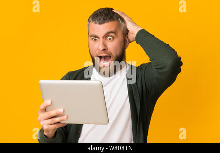 Impressed bearded man holding tablet and touching his head Stock Photo