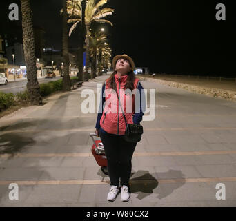 Woman tourist goes at night on the street with a red suitcase Stock Photo