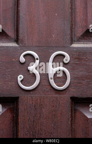 House number 36 in silver metal digits on a red wooden door made out of cherry wood Stock Photo