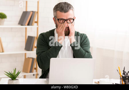 Tired man is working on laptop at home Stock Photo