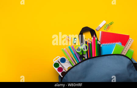Backpack with stationery inside on yellow background Stock Photo