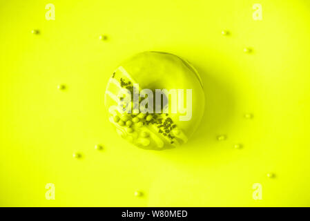 Sweet doughnut with icing on trendy yellow neon color background. Tasty donut over monochrome texture, copy space, top view. Stock Photo
