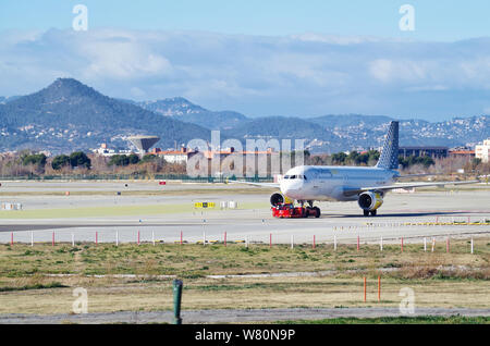 An Airbus A320 plane of Vueling Airlines being towed by Iberia Handling Services in the Barcelo-El Prat Airport (IATA: BCN) Stock Photo