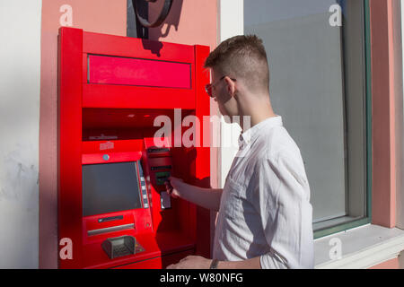 young man student withdrawing money from a bank cash point, outdoors Stock Photo