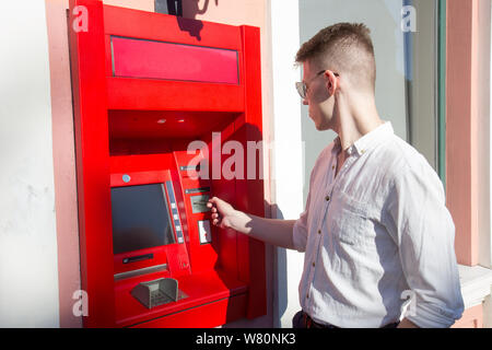 young man student withdrawing money from a bank cash point, outdoors Stock Photo