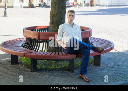Handsome young man sitting on a bench in the town Stock Photo
