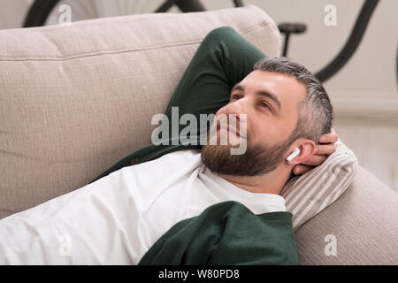 Dreamy caucasian man relaxing on sofa, listening to music Stock Photo