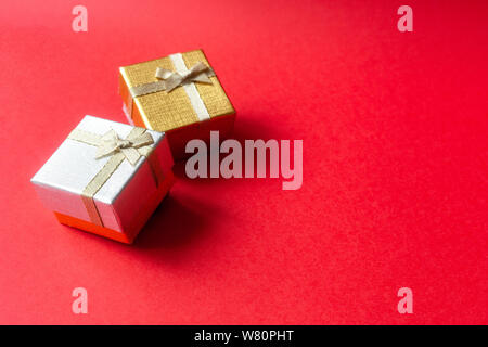 Two New Year's golden and silver gift box with a ribbon tied with a bow on a red background with a place for inscription. Stock Photo