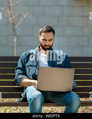 Handsome young manager working on laptop while sitting outdoors on the bench, concept of work life balance Stock Photo