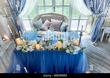 Wedding table decorated with white flowers, candles. Soft sofa with cushions, large window.Blue and white. Stock Photo