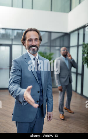 Businessman reaching his hand out to colleague while greeting Stock Photo
