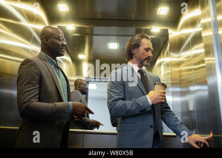 Grey-haired mature businessman pressing button in elevator Stock Photo