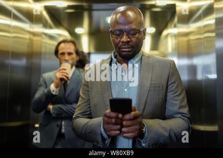 Dark-skinned young businessman reading message on smartphone Stock Photo
