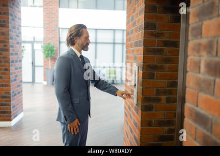 Grey-haired man wearing suit waiting for elevator after meeting Stock Photo