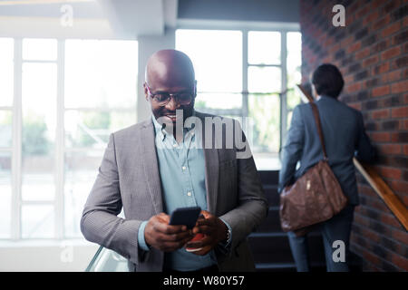 Dark-skinned businessman wearing glasses smiling while reading message Stock Photo