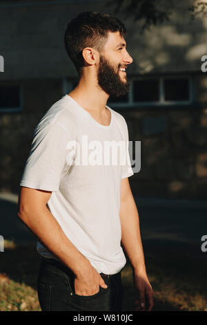 Side view portrait of a adult bearded man looking away laughing in the morning dressed in white shirt and black jeans. Stock Photo