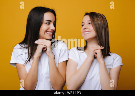 Portrait of two beautiful european female looking emotive and satisfied one to another laughing against a yellow background. Stock Photo