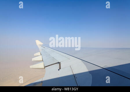 Blurry unclear sky above desert earth surface at troposphere atmosphere viewed from airplane's window located above airplane's wing and jet. Stock Photo
