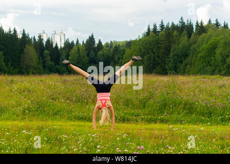 young woman doing somersault cartwheel outdoors in a meadow outside the city Stock Photo