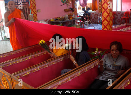 Thais people are seen praying in coffins at Wat Takien temple in Nonthaburi province, on the outskirts of Bangkok.Hundreds of Buddhist believers pay a small fee to lie in pink coffins at 9:00 am and 1:00 pm every day during the unusual daily resurrection service that they believe will wash away bad luck and prolong life. Stock Photo